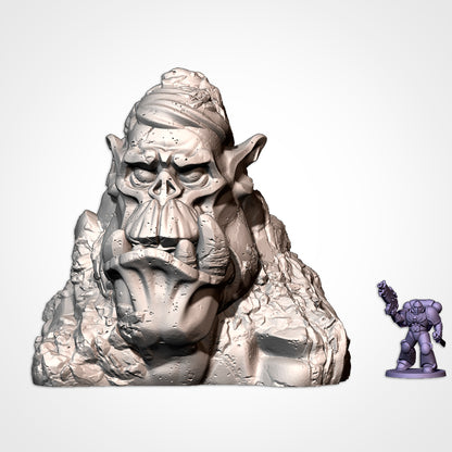 Monument 3: orc head with side-parted hair in a rock outcrop, beside a 32mm figure (Txarli Factory render)