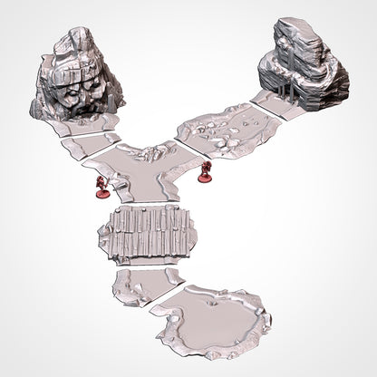 Assembled Modular River System scene: a Y-junction river splitting between two tall rocky spring-source cliffs, crossed by a wooden plank bridge and opening into a lake pool. Unpainted 3D-printed resin water terrain, 32/28/15/8mm tabletop wargaming scenery, designed by Txarli Factory.